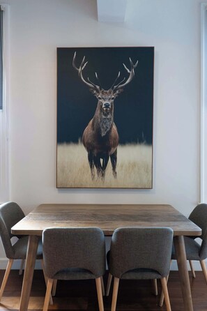 A dining area with a wooden table and four grey chairs, a framed wildlife painting on the wall, and a window with curtains. - Vibrant Darlinghurst Inner City Oasis (Darlinghurst)