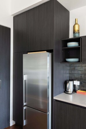 A modern kitchen with dark cabinetry, a stainless steel refrigerator, a coffee maker, and a shelf with plates. - Vibrant Darlinghurst Inner City Oasis (Darlinghurst)