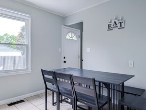 Un espace repas comprenant une table et des chaises, une fenêtre, une porte et un panneau fixé au mur.