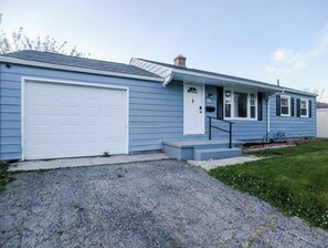 A two-story house with a white garage door, a front porch with a small set of steps, and a mailbox.