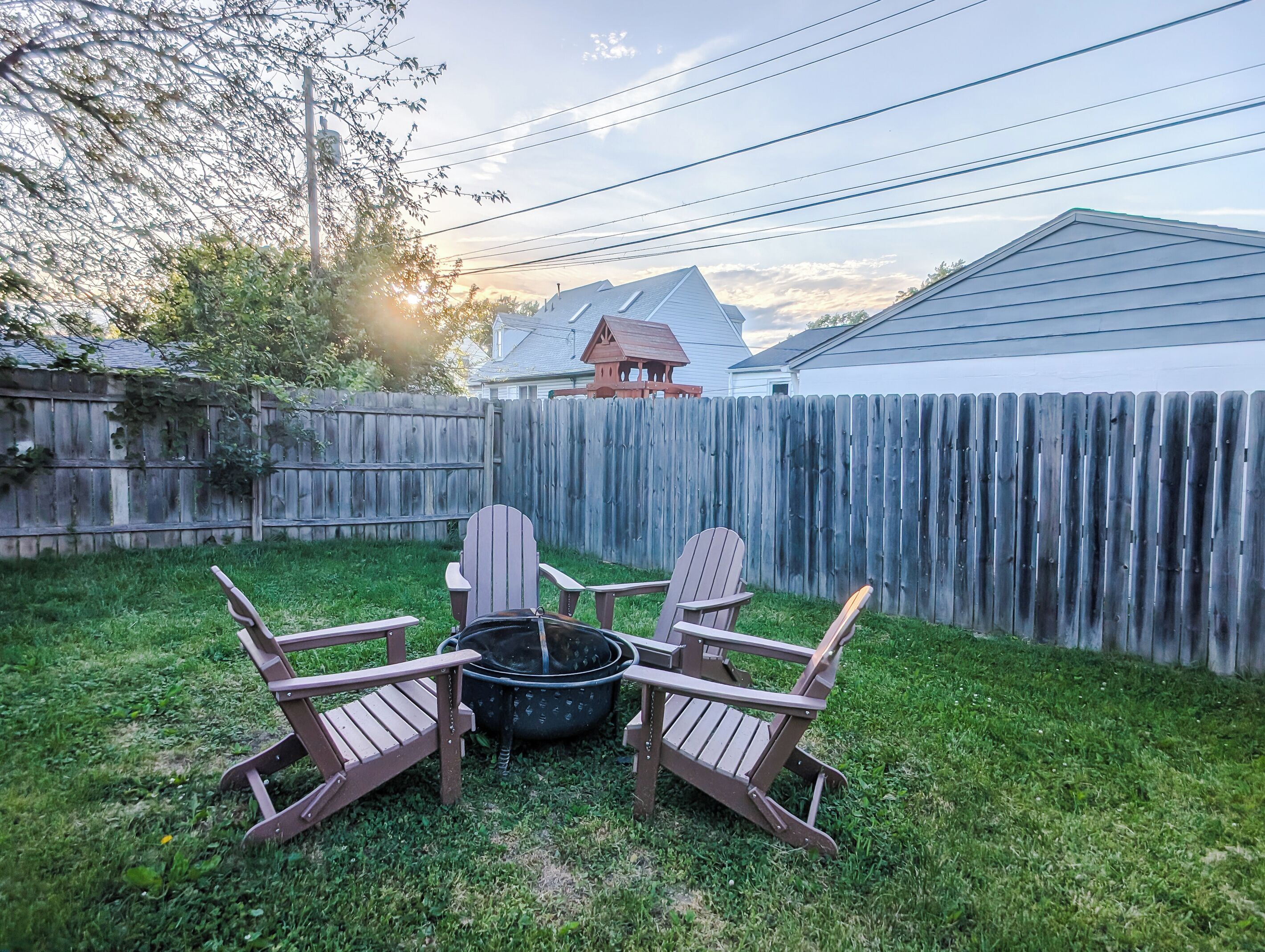 Un jardin avec une clôture en bois, un foyer et des fauteuils Adirondack.