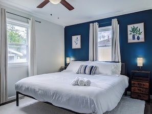 Un lit bien fait, avec du linge de lit blanc, un ventilateur de plafond et une table de chevet avec une lampe.
