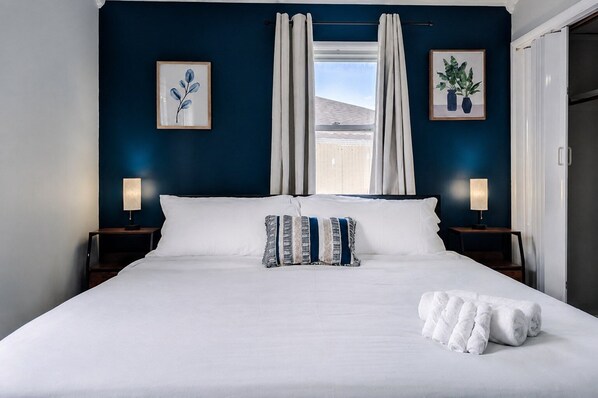 A hotel room with a large bed, two bedside tables with lamps, and two framed artworks on the wall.