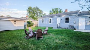 A backyard with a lawn, a wooden deck, and Adirondack chairs.