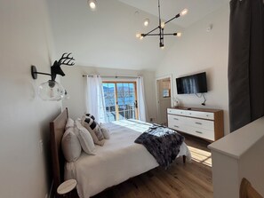 Un dormitorio con cama, cómoda, televisor y vistas al exterior.