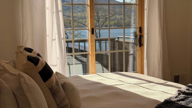 Een bed met uitzicht op een meer en bergen door een raam.