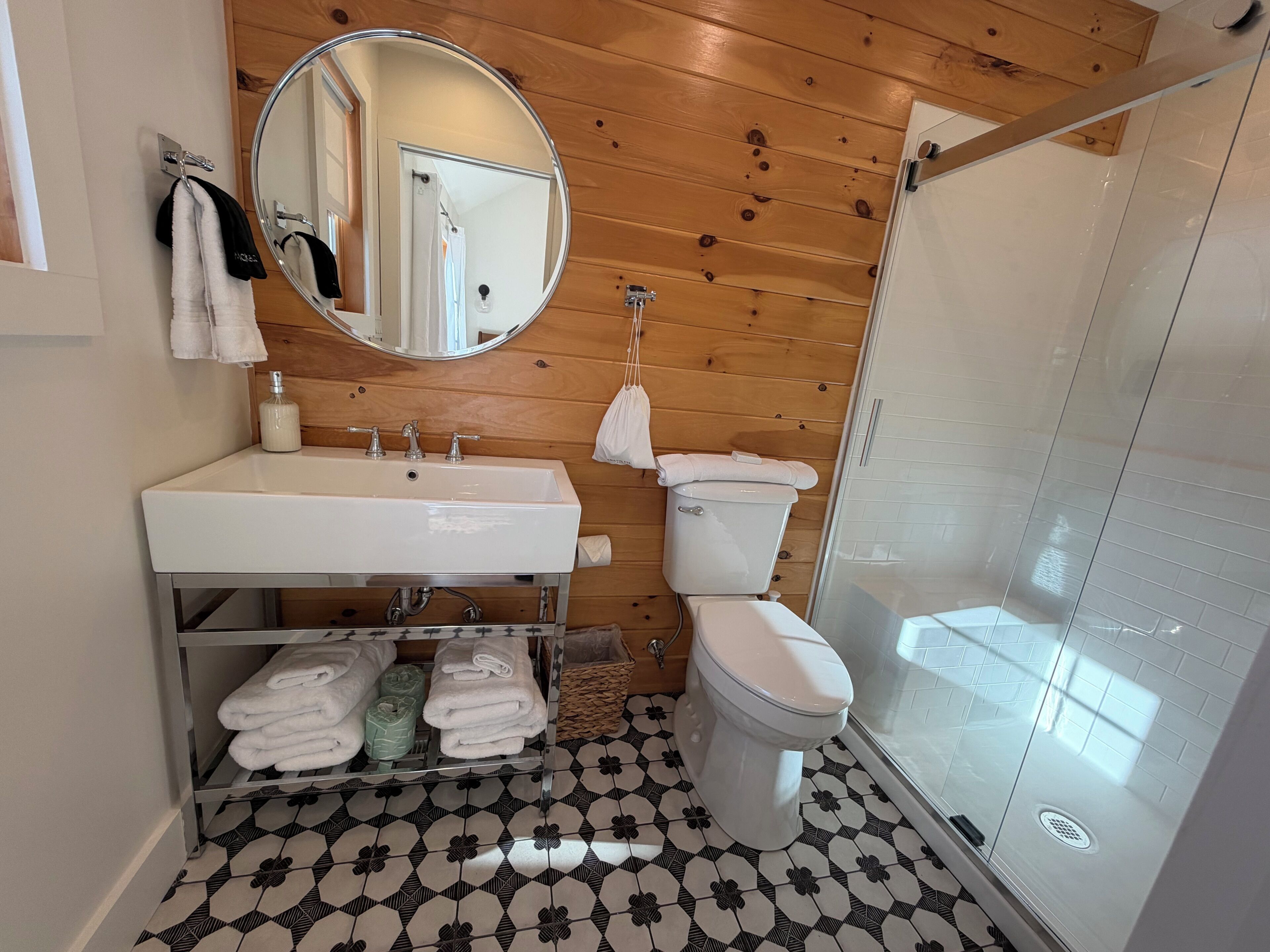 Une salle de bain avec un plafond en bois, un lavabo blanc, des toilettes et une cabine de douche en verre.