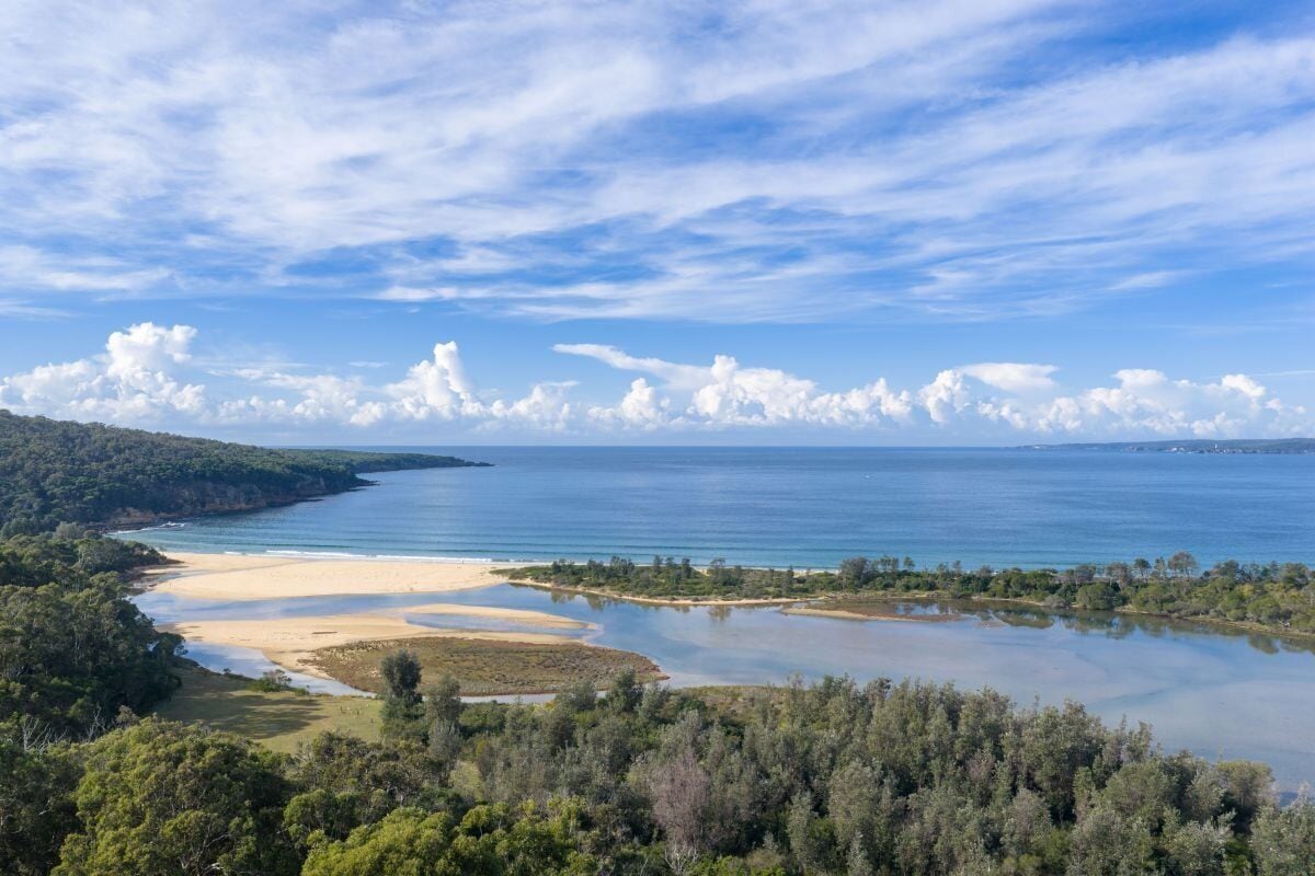 Un paysage côtier comprenant une plage, de l’eau et des collines boisées.