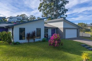 Une maison moderne à deux étages, dotée d’un garage, d’une pelouse bien entretenue et d’une variété de plantes.