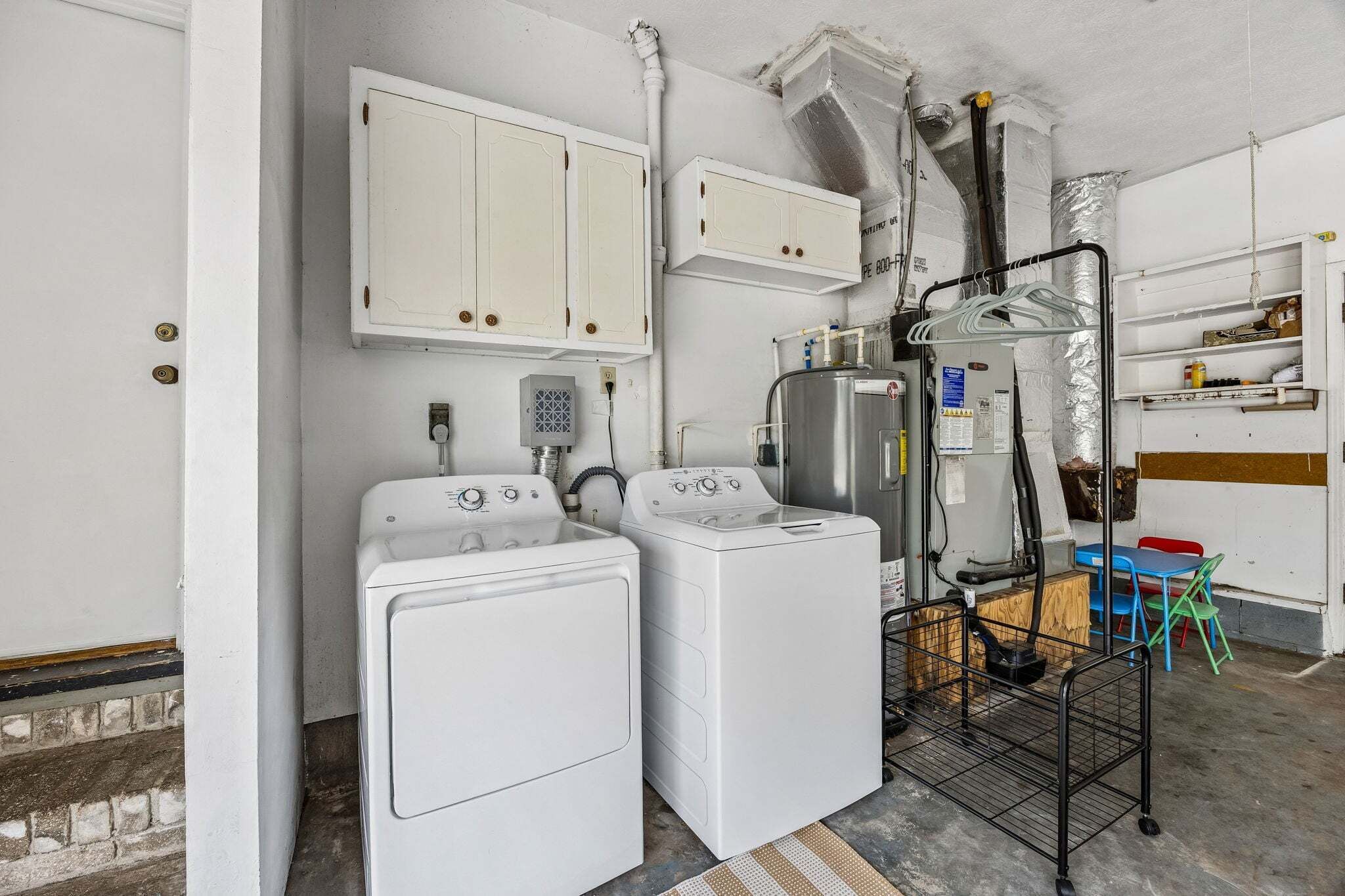 A laundry area with two white washing machines, a dryer, a metal rack, and a small table with chairs.