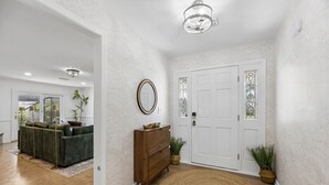 A hallway with a wooden floor, a green sofa, a wooden dresser, and a white door with a glass panel. - The Southwind|Pool|3-Min Drive to Beach|Sleeps 10 (St. Augustine)