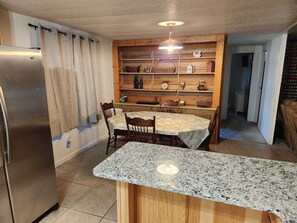 A kitchen with a granite countertop, wooden cabinets, a stainless steel refrigerator, and a dining area with chairs and a table.