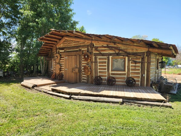 A rustic log cabin with a wooden door, a window, and a porch with wooden steps.