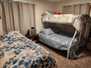 Ein Zimmer mit zwei Betten, eines mit Baldachin und eines ohne, einem kleinen Tisch mit Fernseher und Vorhängen an den Fenstern.