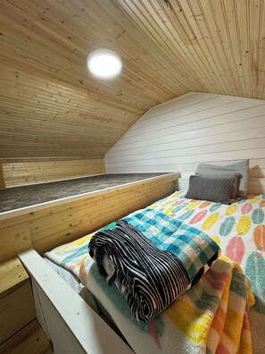 Una habitación pequeña y acogedora con techo inclinado, una cama con un edredón colorido, una almohada y un banco.