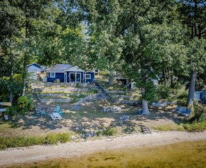 Ein Haus mit Veranda, umgeben von Bäumen und einem Feldweg, der zu Sitzgelegenheiten im Freien führt.