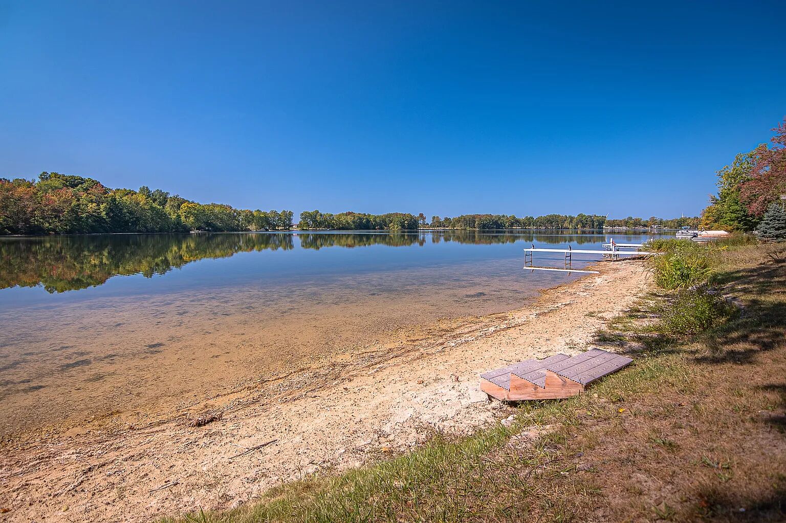 Vista de un lago con agua cristalina, un muelle de madera y una orilla cubierta de césped.
