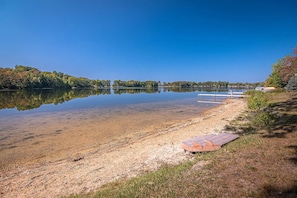 Blick auf einen See mit klarem Wasser, einer Holzsteg und einer grasbewachsenen Uferlinie.
