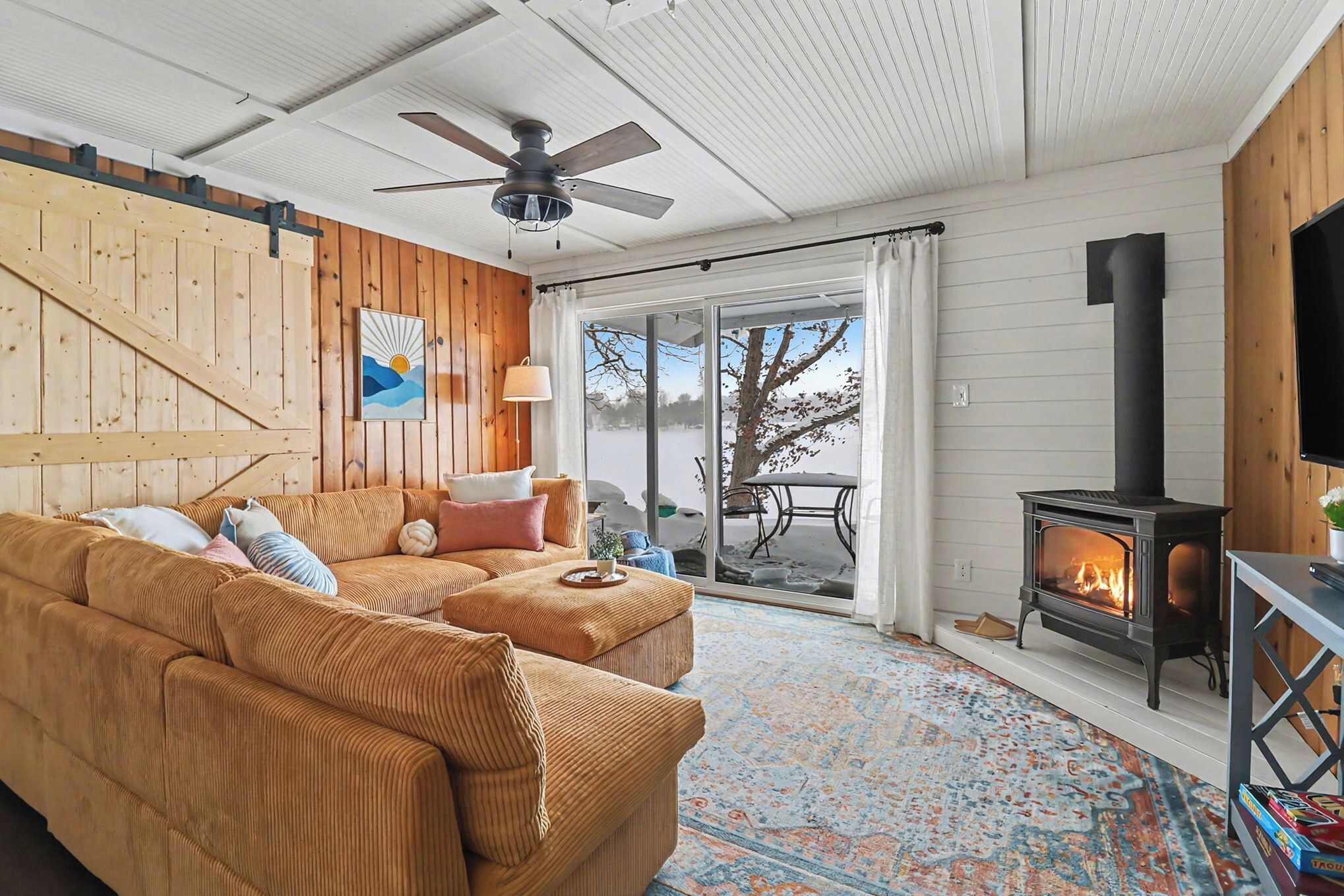 Un salón acogedor con un sofá grande, una chimenea y vistas a través de un ventanal.