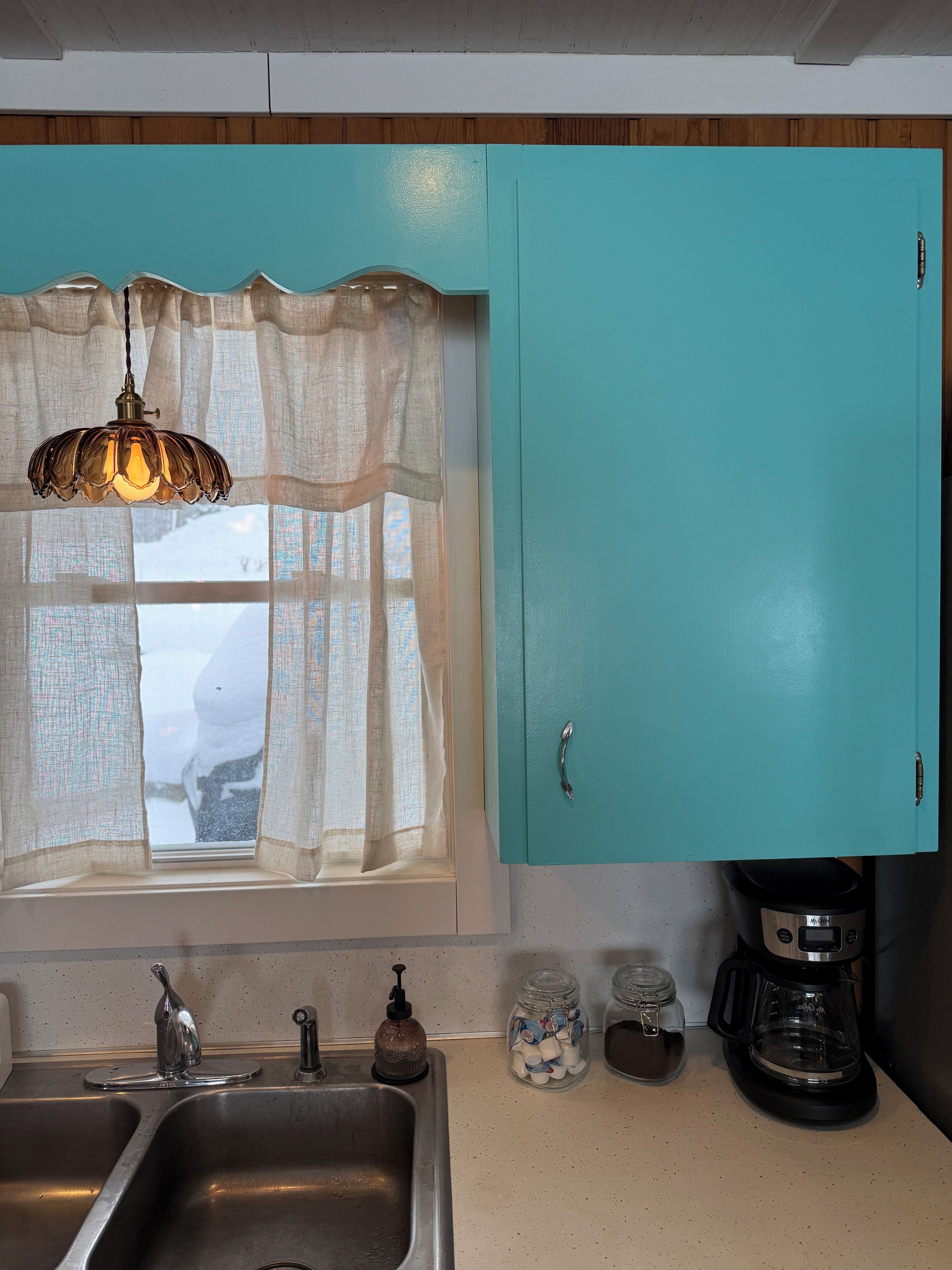 A kitchen with a window, a sink, a coffee maker, and cabinets.