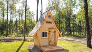 Una cabaña de madera pequeña con techo a dos aguas, una puerta y una ventana, rodeada de un bosque.