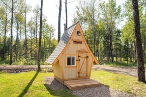 A small wooden cabin with a pitched roof, a door, and a window, surrounded by a forest. - Flowing Waters Retreat - Two Cabins with Sauna (Two Harbors)