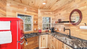 Una cocina compacta con paredes de madera, un refrigerador rojo, un lavamanos y una estufa.