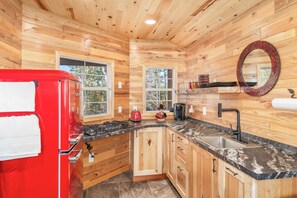 A compact kitchen with wooden walls, a red refrigerator, a sink, and a stove. - Flowing Waters Retreat - Two Cabins with Sauna (Two Harbors)