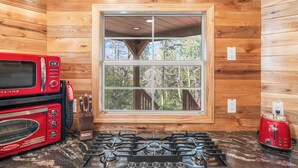 Una cocina con estufa a gas, un tostador rojo y una ventana con vistas a árboles.