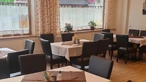 A restaurant with multiple tables and chairs, large windows with curtains, and a view of a building outside.