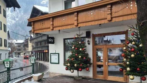 A hotel with a wooden balcony, two Christmas trees, and a sign that reads 'Sky.'