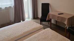 A hotel room with two beds, a chair, a table with a remote control, a television on the wall, and a window with curtains.