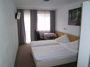 A hotel room with a bed, a desk, a chair, a painting on the wall, and a window with curtains.