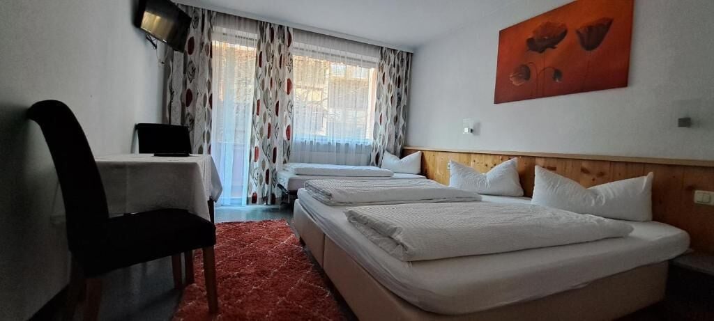 A hotel room with a desk, two beds, a red carpet, and a painting on the wall.
