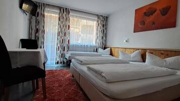 A hotel room with a desk, two beds, a red carpet, and a painting on the wall.