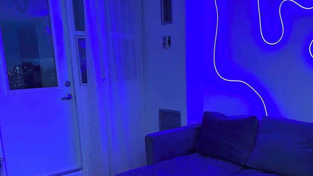 Una sala moderna con un sofá seccional, un tapete estampado y una luz de neón decorativa en la pared.