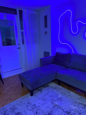 A modern living room with a sectional sofa, a patterned rug, and a neon light design on the wall. - Sunny Modern 1BR | Quiet
Islington Stay (Toronto)