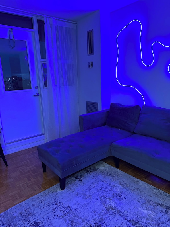 A modern living room with a sectional sofa, a patterned rug, and a neon light design on the wall.