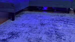 Una sala de estar moderna con un sofá seccional, un tapete estampado y una pared con un diseño de luz de neón azul.