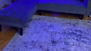 Una sala de estar moderna con un sofá seccional gris, un tapete blanco con textura e iluminación de neón azul en la pared.