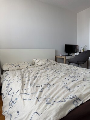A bedroom with a bed, a desk with a computer, and a chair.
