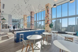 Ein modernes Interieur mit einer zentralen Bar, runden Tischen und hohen Decken mit geometrischen Leuchten.