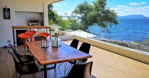 A dining area with a wooden table and black chairs, a grill, and a view of the sea. - Incredible apartment on the shores of Lake Villarrica!!! fully equipped!!! (Pucon)