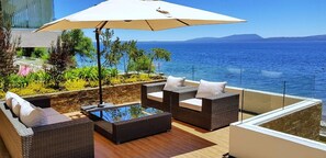 Un balcon agrémenté de meubles en osier, d’une table en verre et d’un grand parasol.