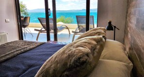 Ein Schlafzimmer mit Meerblick, einem Bett, einem Sessel und einer Lampe.