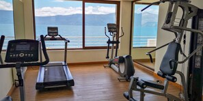Une salle de sport équipée d’appareils de cardio, d’un tapis de course et d’un vélo elliptique, avec vue sur une étendue d’eau et des montagnes au loin.