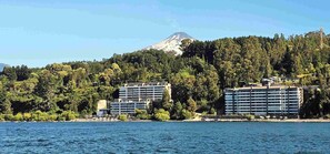 Ein Hotel an der Küste mit mehreren Etagen, einem Berg im Hintergrund und freiem Blick auf das Meer.