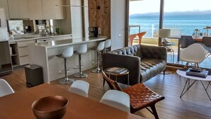 A modern kitchen with a view of the sea, a dining area with a table and chairs, and a seating area with a sofa and chairs. - Incredible apartment on the shores of Lake Villarrica!!! fully equipped!!! (Pucon)