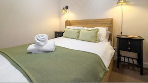 A neatly made bed with a green blanket, two bedside lamps, and a wooden headboard. - Cosy 2 Bed Viking Bay Cottage (Broadstairs)