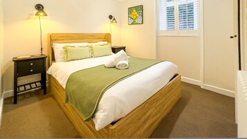 Uma cama bem arrumada com um cobertor verde, duas luminárias de cabeceira, uma mesa de cabeceira e uma janela com persianas.